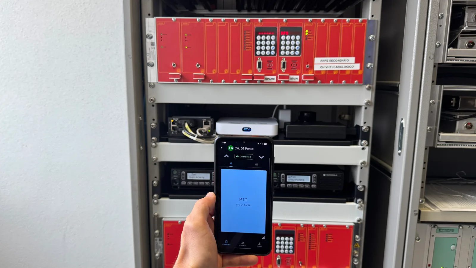 Smartphone con l’app Respondr in push-to-talk, davanti al rack con il gateway radio e gli apparati